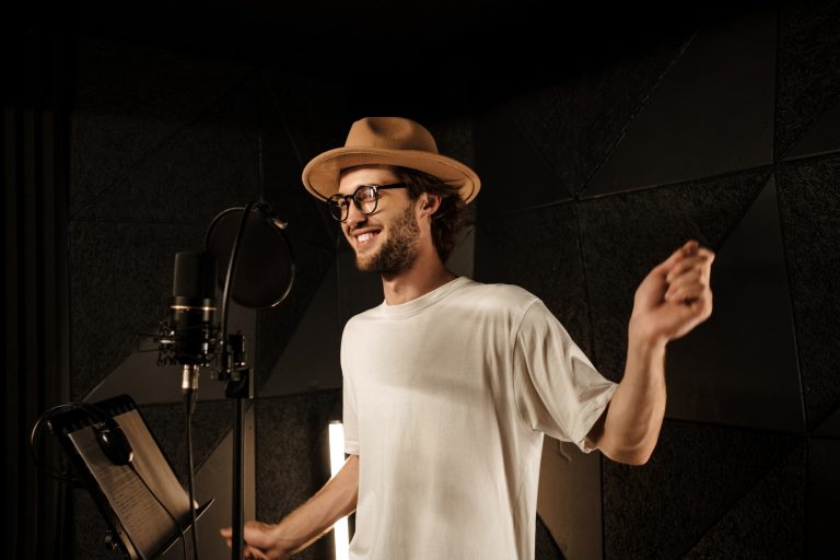Handsome stylish musician in hat happily dancing recording new song in sound studio